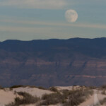 The dunes and mountains beyond start to show the colors of the setting sun.